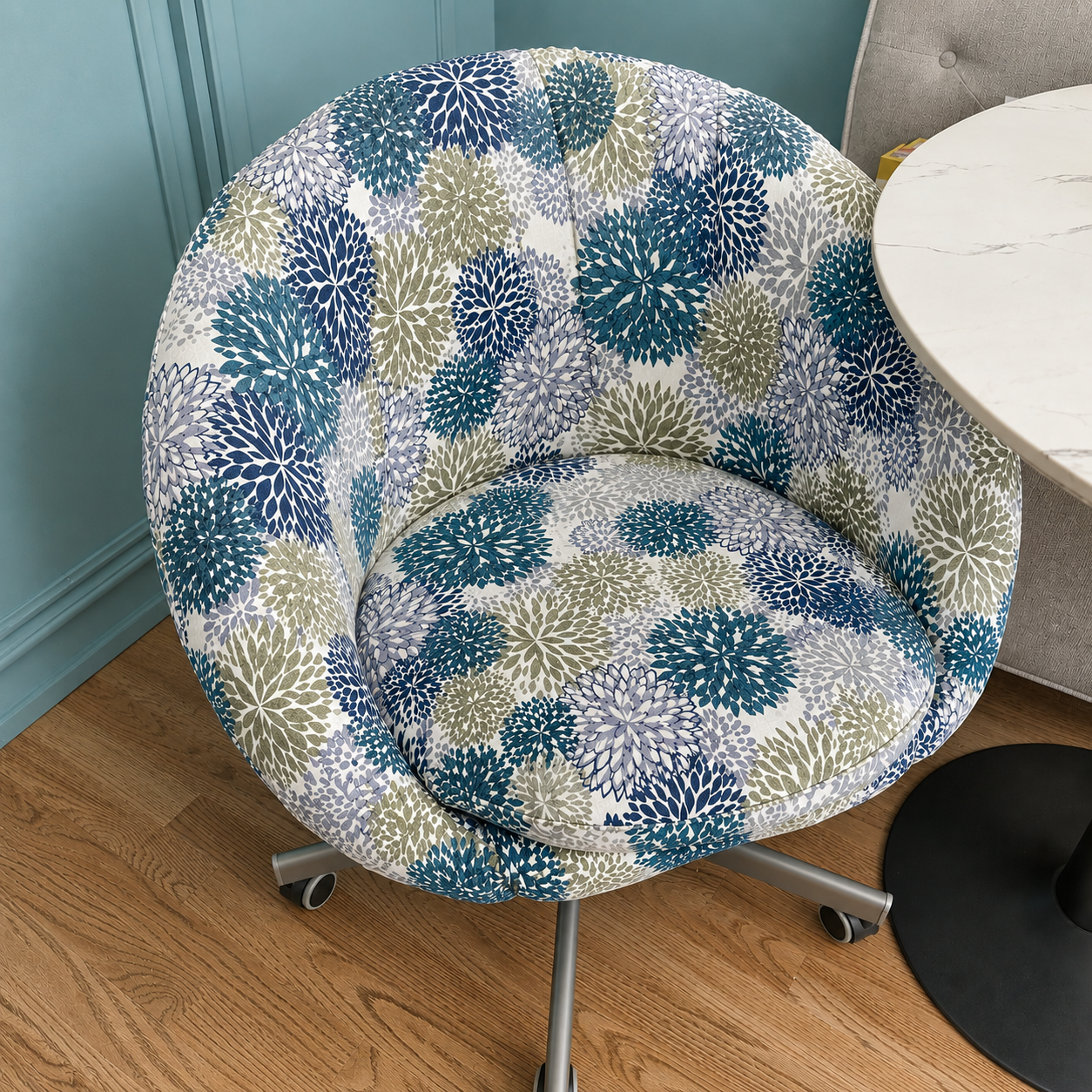Chair with a floral patterned cover on a wooden floor against a blue wall.
