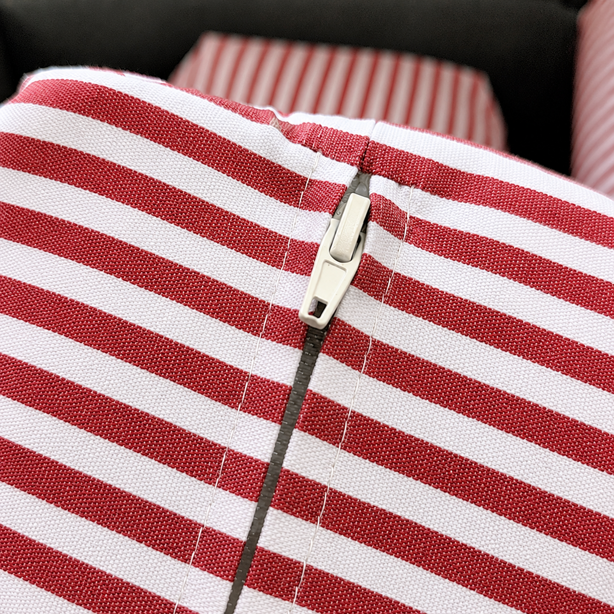 Close-up of a red and white striped fabric item with a silver zipper pull, showing the texture of the woven material.