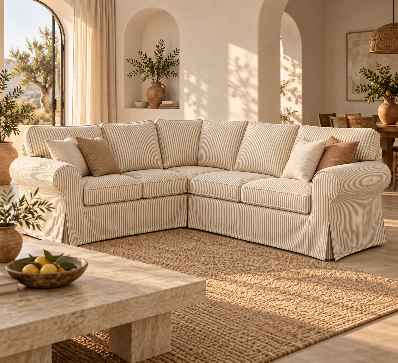 A cream-colored sectional sofa with vertical striped upholstery, styled in a warm, sunlit Mediterranean-inspired living room with beige walls, a woven rug, and neutral throw pillows.