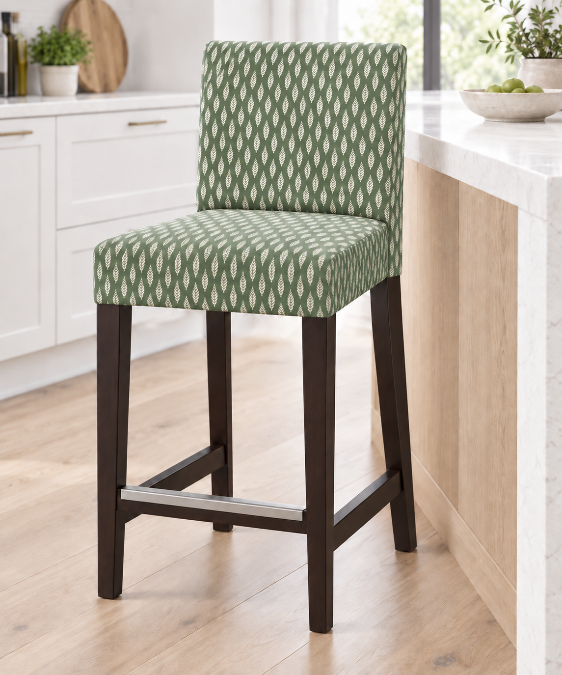 A bar stool with a green and white geometric patterned fabric upholstery and dark brown wooden legs, positioned in a bright, modern kitchen setting.