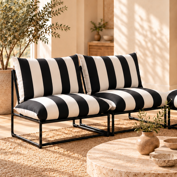 A modern outdoor sectional sofa set with black and white striped cushions and black metal frames, arranged in a warm, sunlit patio lounge area with a round stone coffee table and woven rug.