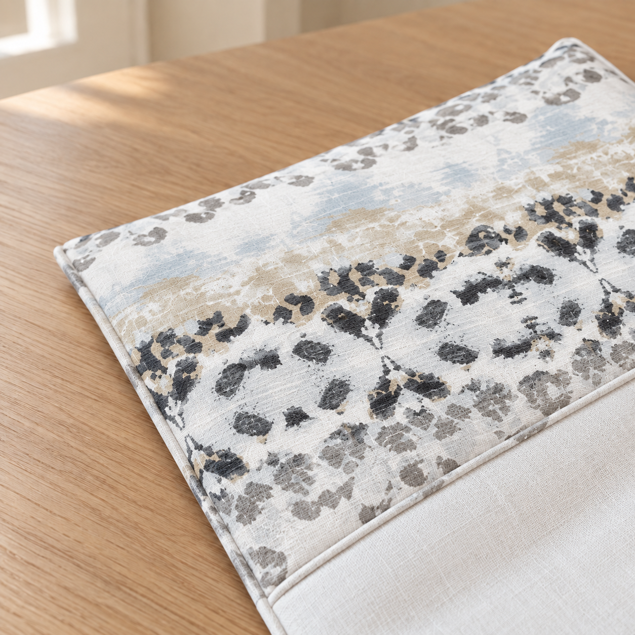A kids Poang cushion cover with an abstract painterly pattern in beige, gray, black, and soft blue, resting on a light wood table.
