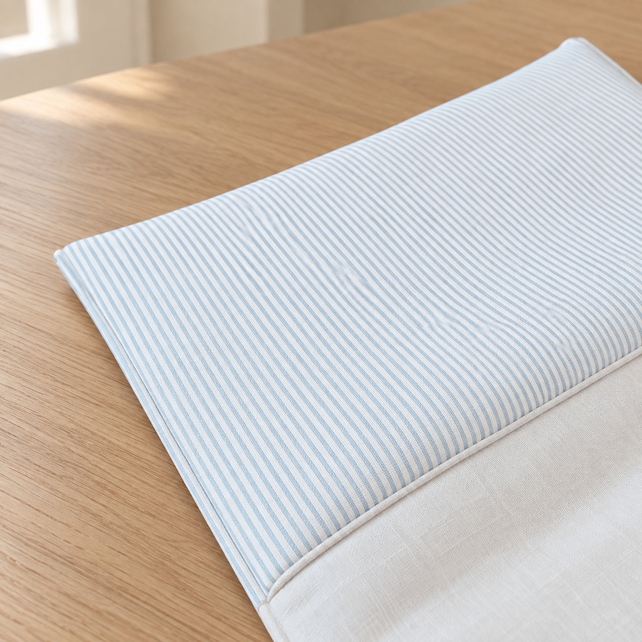 A folded light blue and white striped chair cushion cover with a solid white underside, displayed on a light wood table.