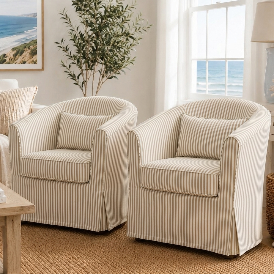 Two matching slipcovered armchairs with vertical cream and beige stripes, shown in a bright coastal-style living room.