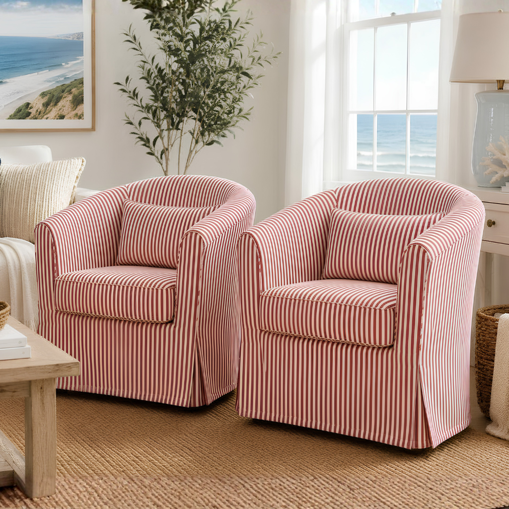 Two matching slipcovered armchairs with pink and white vertical stripes, shown in a bright, coastal-themed living room setting.