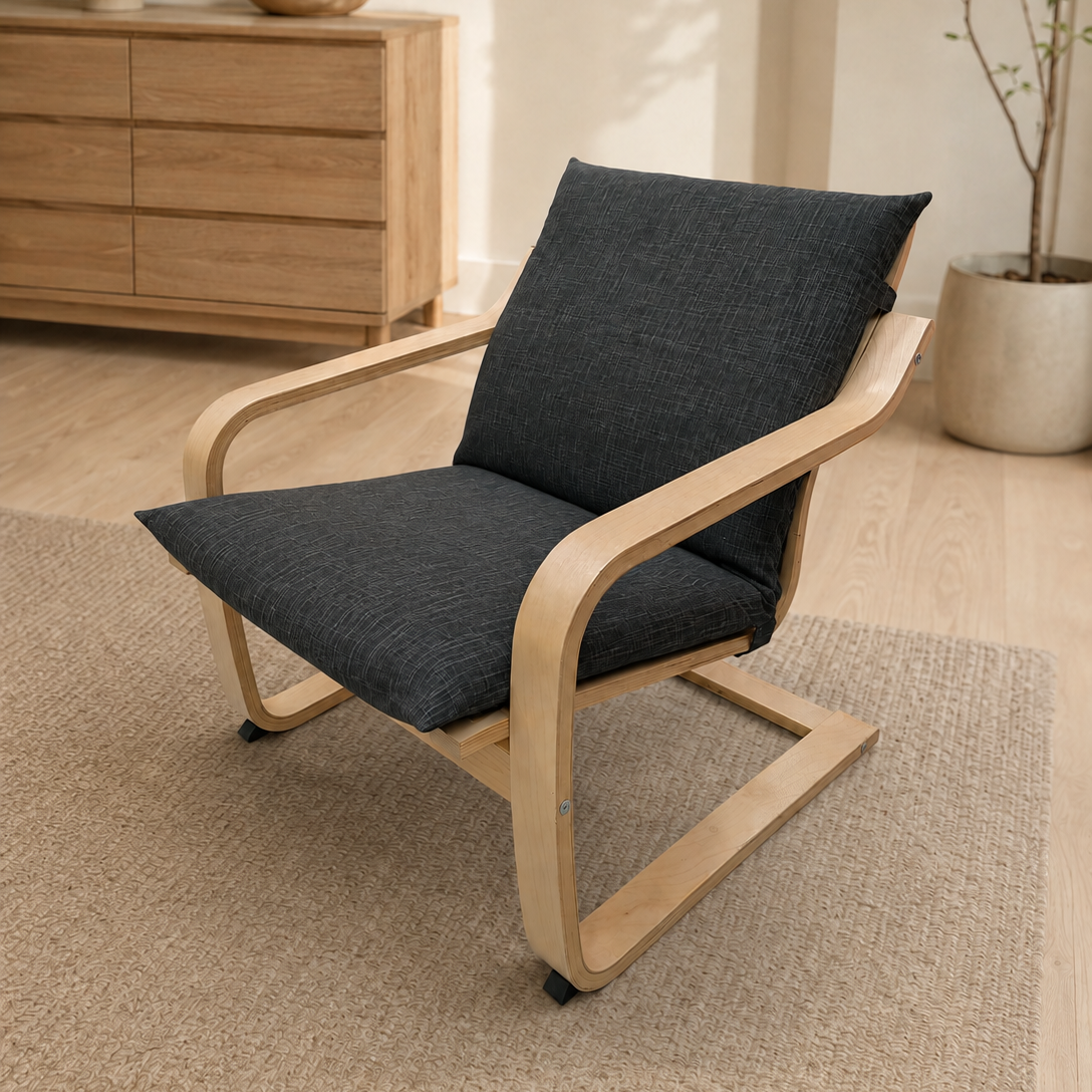 A modern lounge chair with a light natural wood frame and dark charcoal gray fabric cushions, placed on a textured beige rug in a bright, minimalist room.