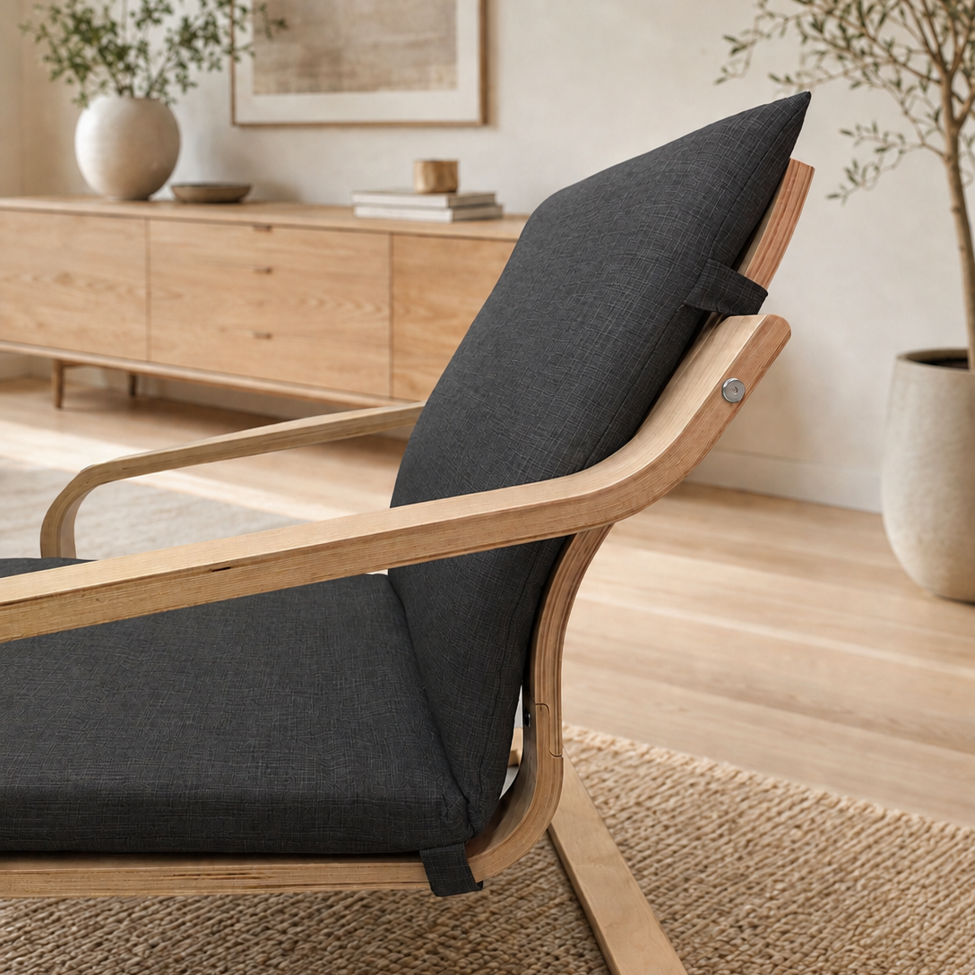 A modern wooden lounge chair with dark gray fabric cushions, shown in a warm, contemporary living room setting with a wooden sideboard and plants in the background.