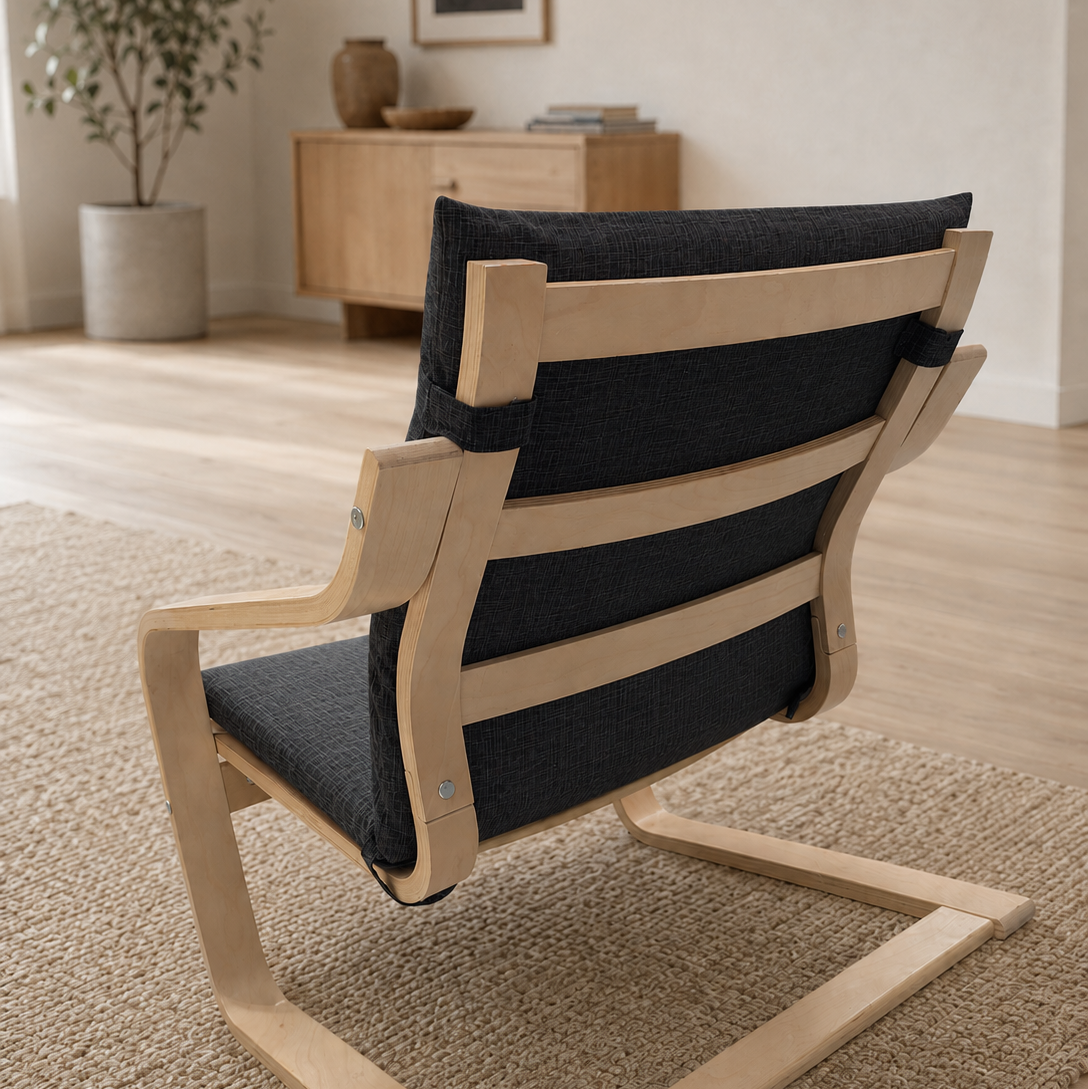 A modern wooden lounge chair with a curved light natural wood frame and dark charcoal gray fabric seat and back cushions, shown in a styled living room setting on a woven rug.