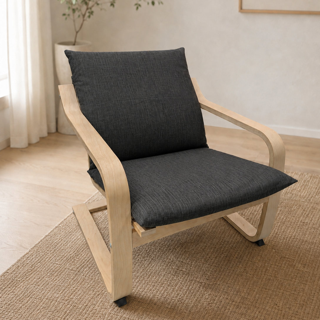 A modern wooden armchair with a dark gray textured seat cushion and backrest cushion, placed on a woven jute rug in a bright, minimalist room.