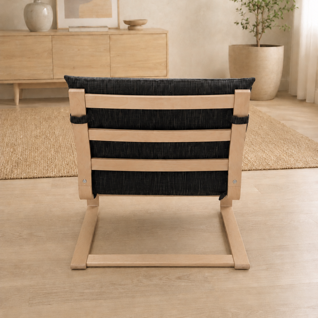 A modern wooden lounge chair with a black woven seat and backrest, shown from the back in a minimalist, warm-toned living room setting.