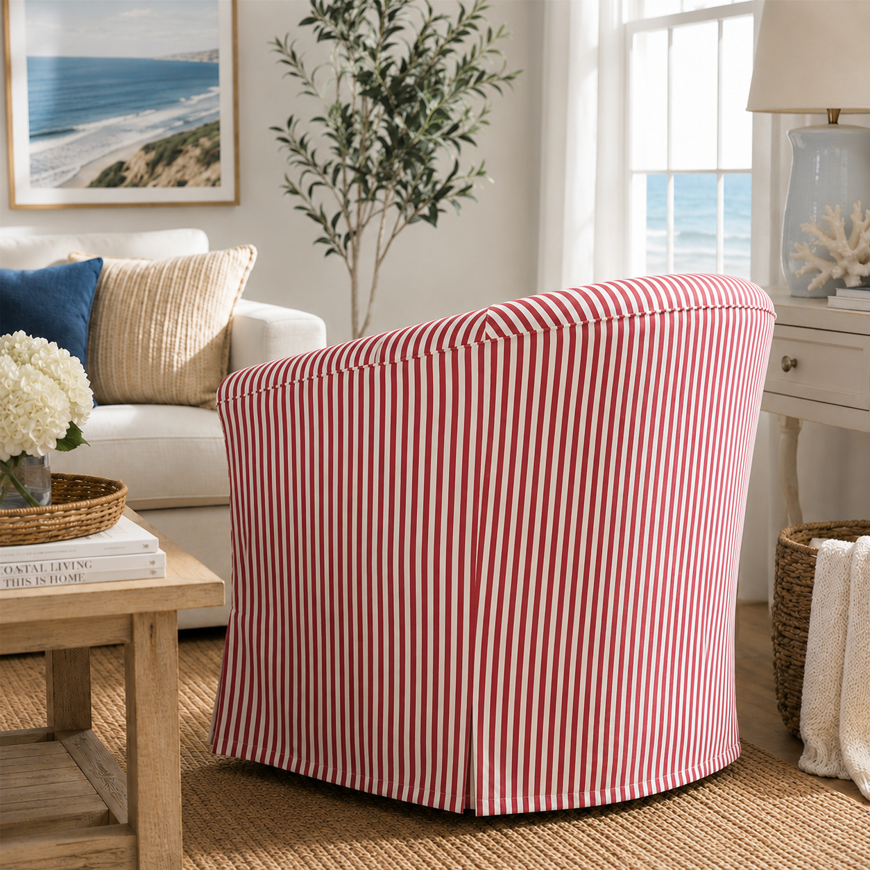 A slipcovered barrel chair with vertical red and white stripes, styled in a bright, coastal-themed living room next to a white sofa and window.