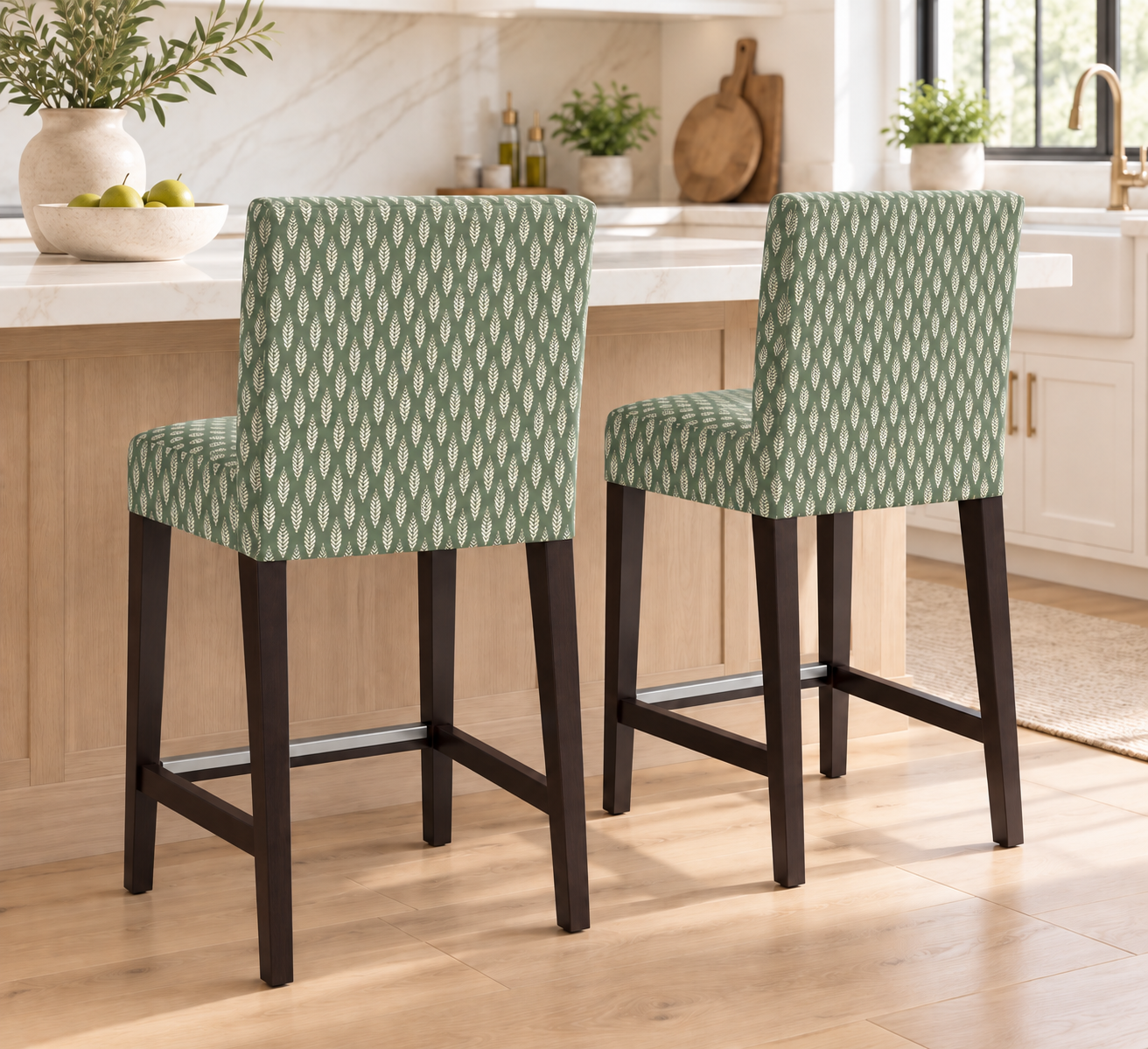 Two counter height bar stools with green and white geometric patterned upholstery and dark wood legs, shown in a bright kitchen setting.