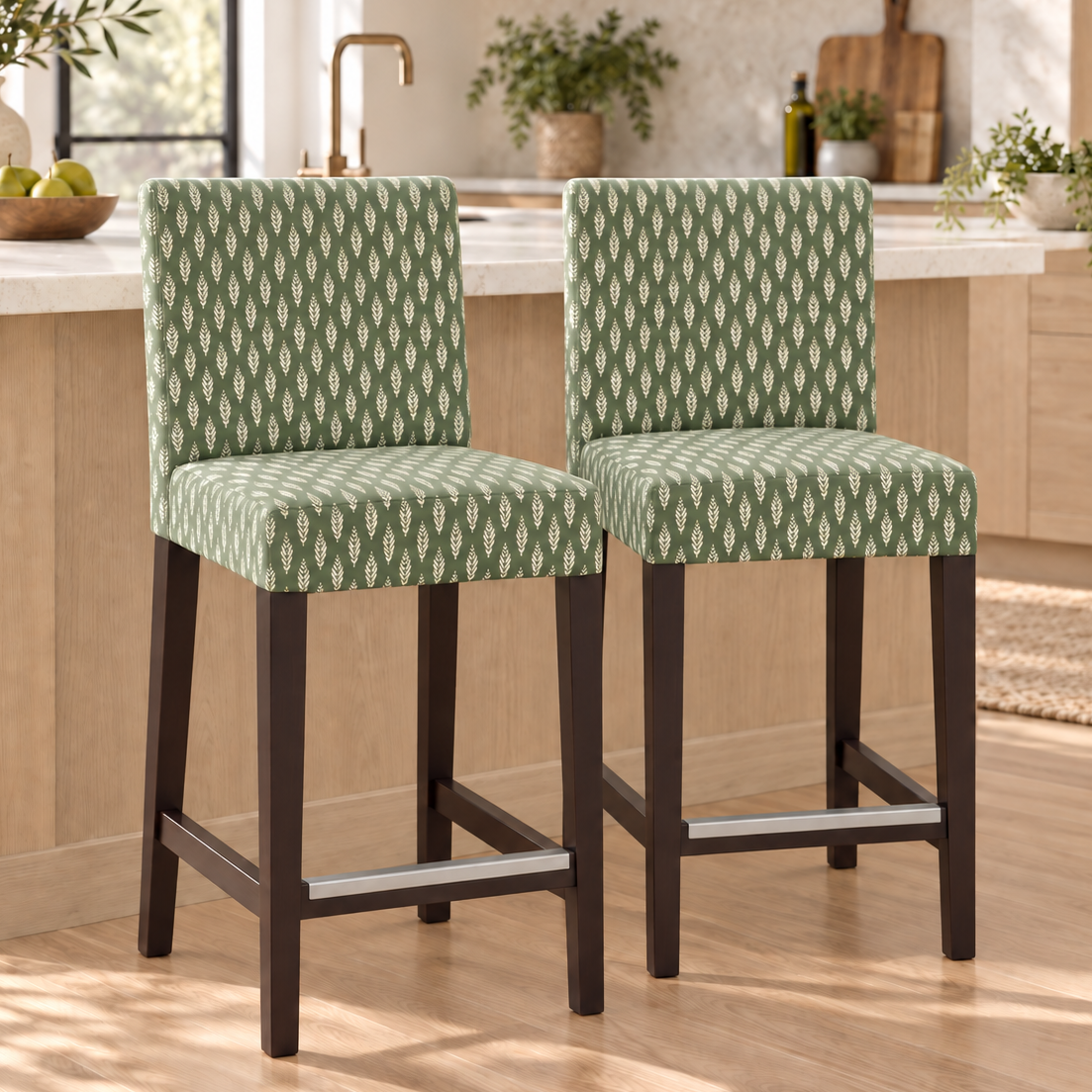 Two upholstered bar stools with green and white geometric patterned fabric and dark wood legs, shown in a bright modern kitchen setting.