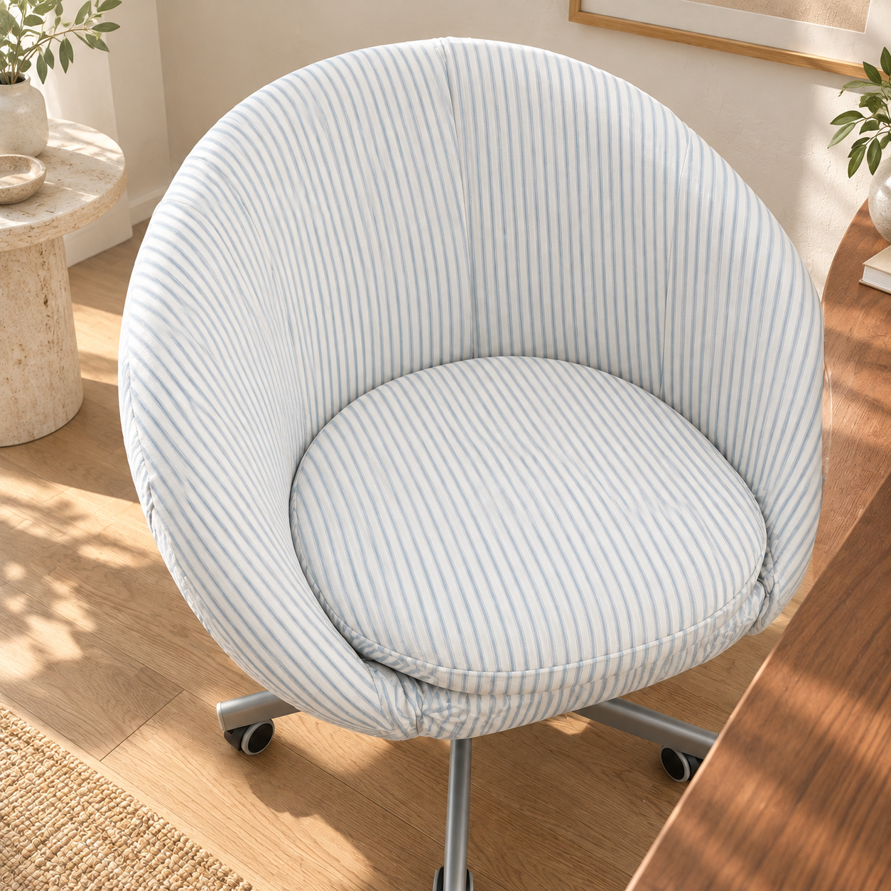 A round upholstered swivel chair with a pale blue and white striped fabric, shown in a bright home office setting with a wooden desk and warm sunlight.