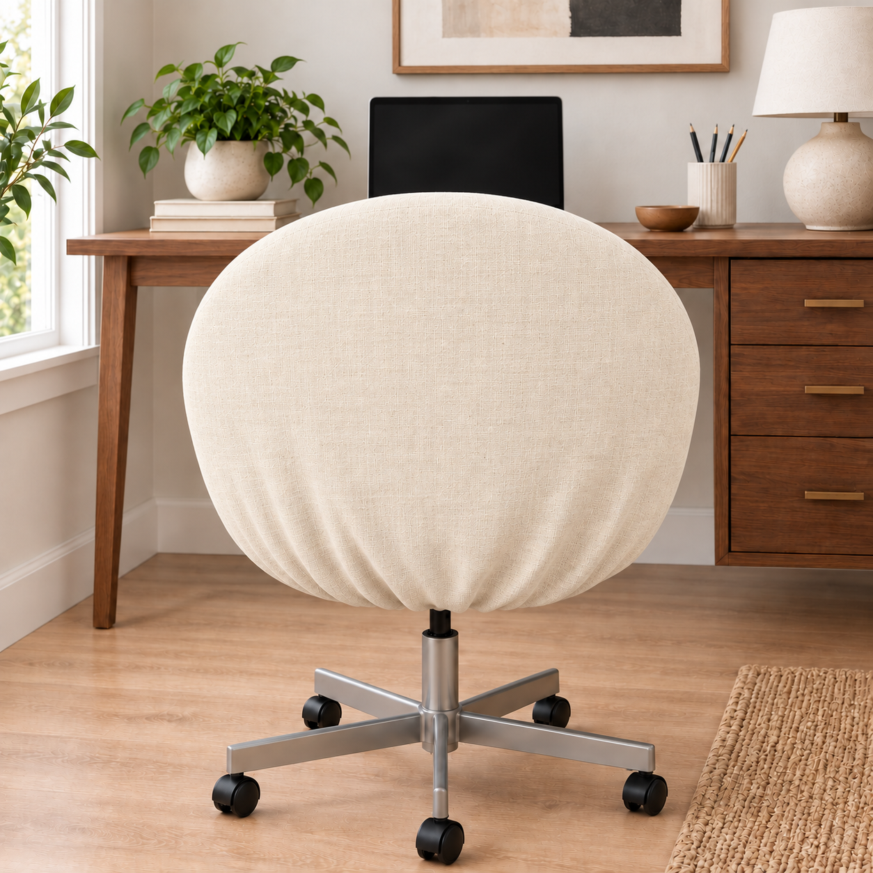 A round upholstered swivel chair in off-white fabric with a silver metal five-star base and black casters, shown in a bright home office setting with a wooden desk, plants, and a lamp.