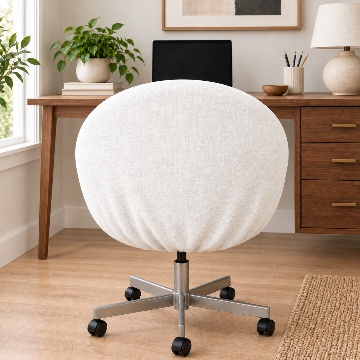 A round upholstered swivel chair in off-white fabric with a silver metal five-star base and black casters, shown in a bright home office setting with a wooden desk, plants, and a lamp.