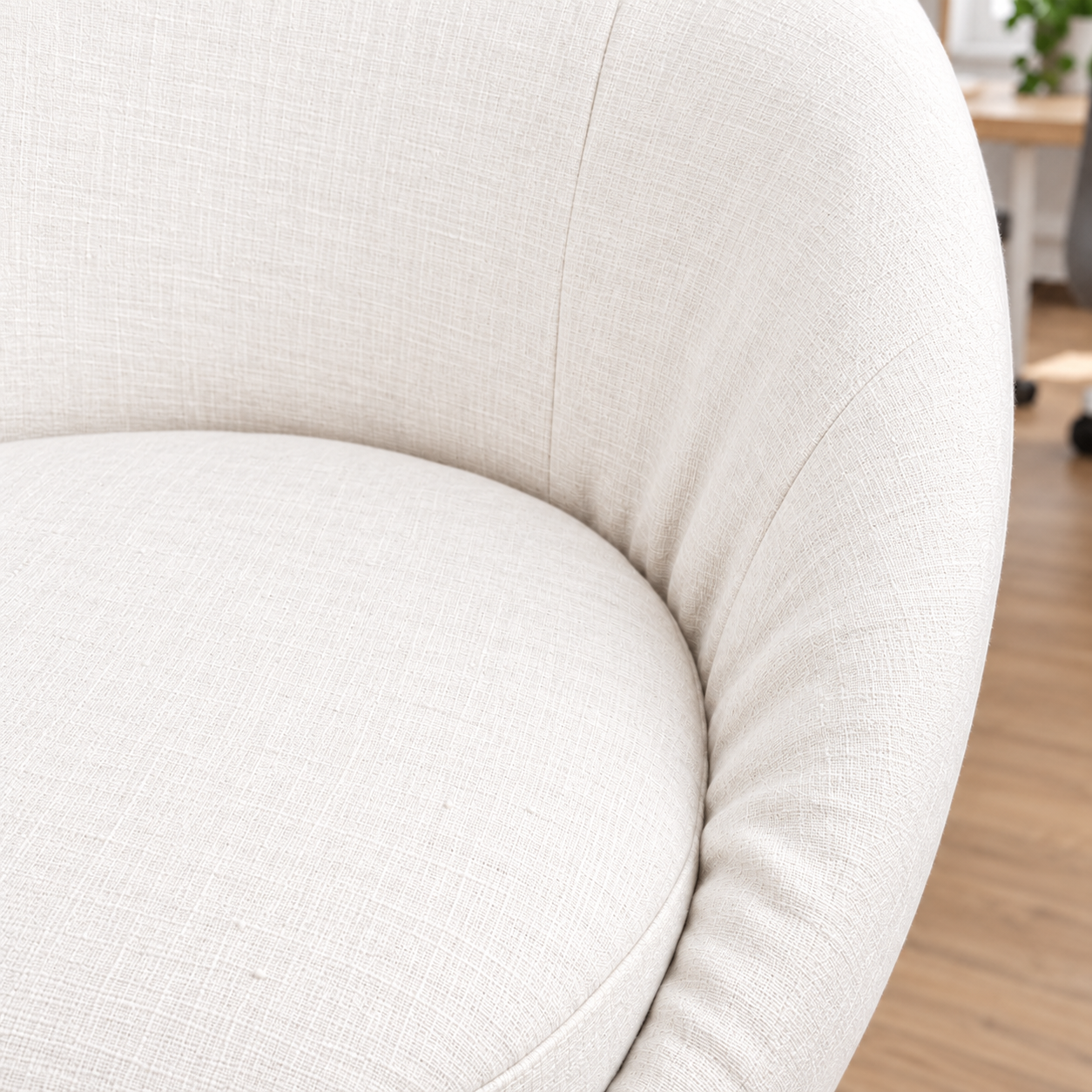 Close-up of a curved upholstered chair or sofa in a light warm off-white fabric, showing the seat and back cushion with a subtle woven texture.