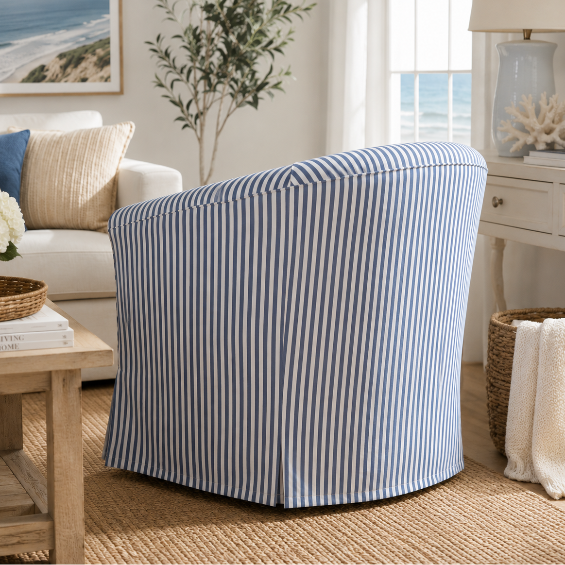 A slipcovered armchair with vertical blue and white stripes, styled in a bright, modern living room with a white sofa, wooden coffee table, and ocean view window.