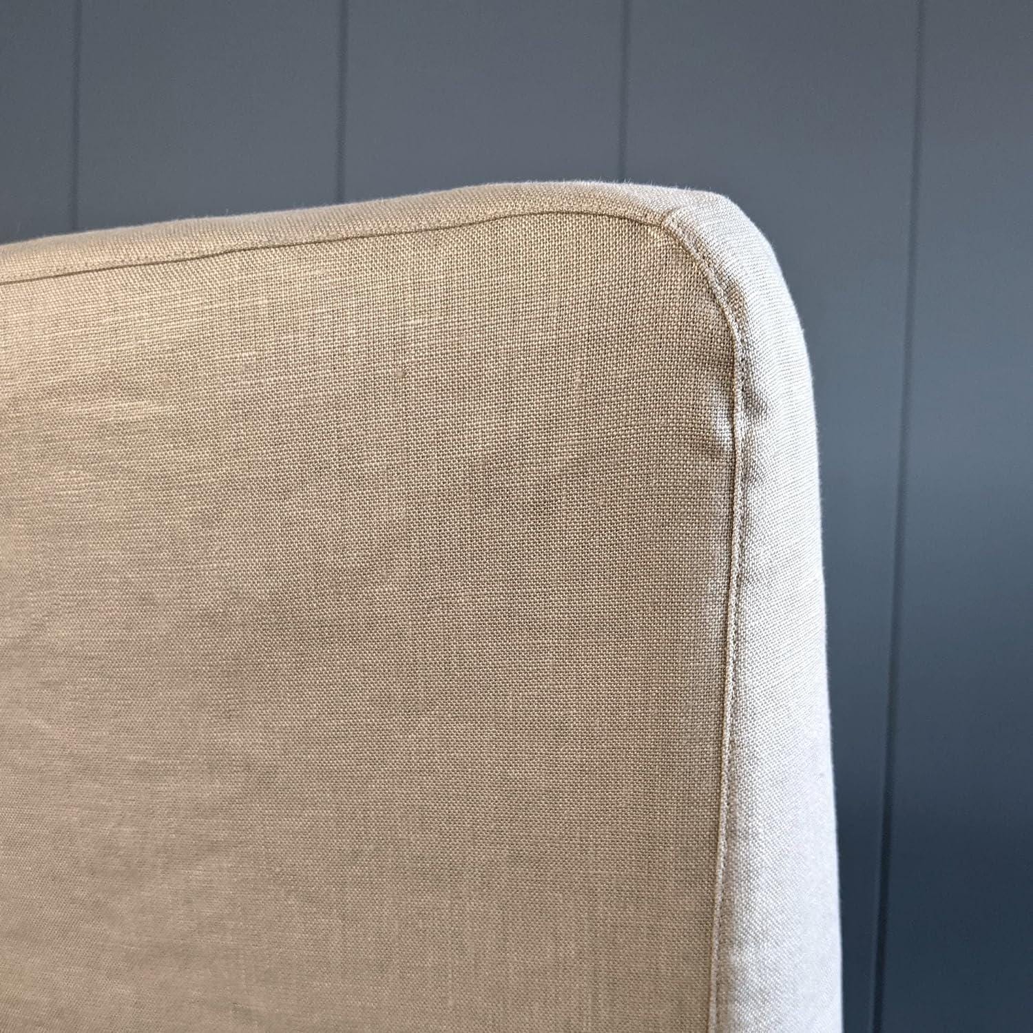 Close-up of a beige upholstered chair against a dark blue wall.