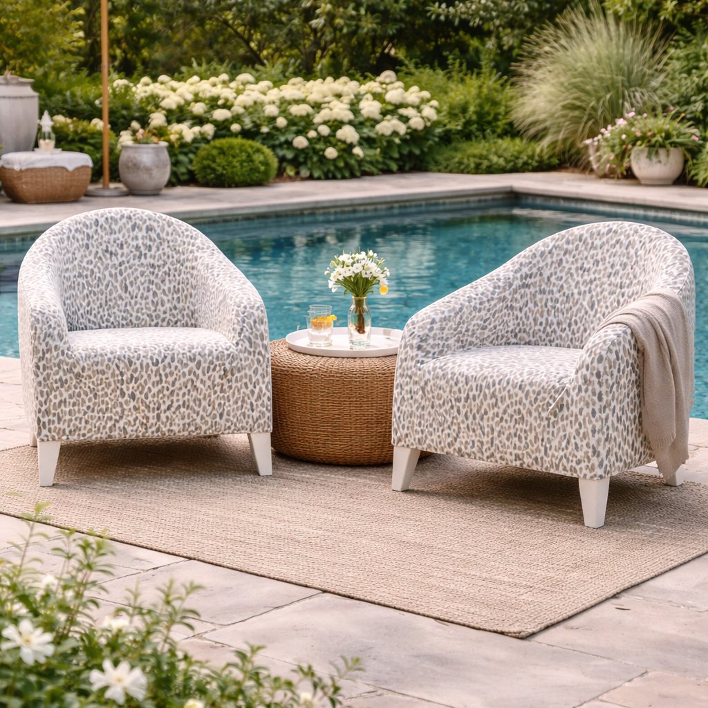 Two patterned chairs with a small table by a poolside, surrounded by greenery.